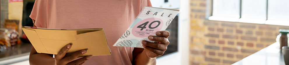 A woman reading a direct mail advertising piece promoting a sale.