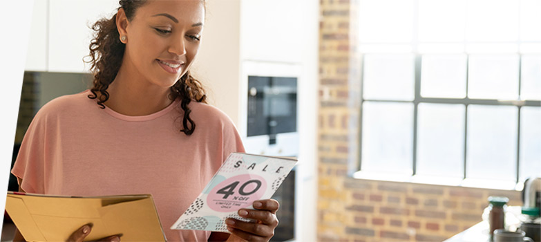 A woman reading a direct mail advertising piece promoting a sale.