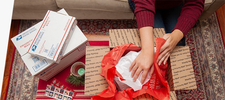 Young woman preparing holiday gifts and Priority Mail boxes to ship for December 25 delivery.