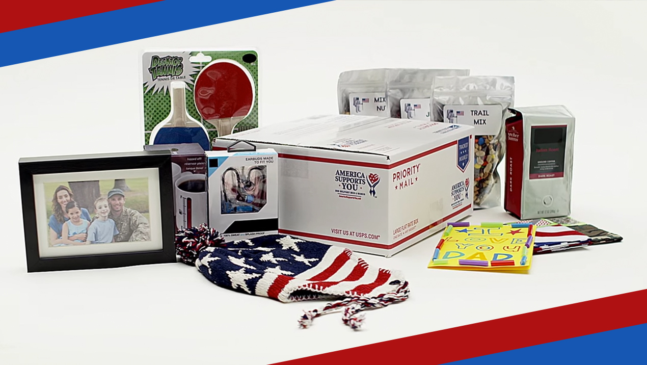 A Priority Mail box surrounded by items that can be shipped inside it including a family photo, a hat designed to look like an American flag, game paddles, birthday cards, trail mix, coffee, and small electronics.