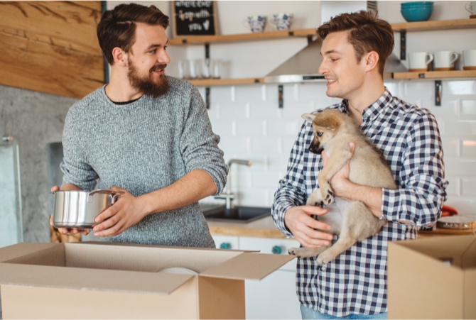 Two people packing boxes while holding a puppy.