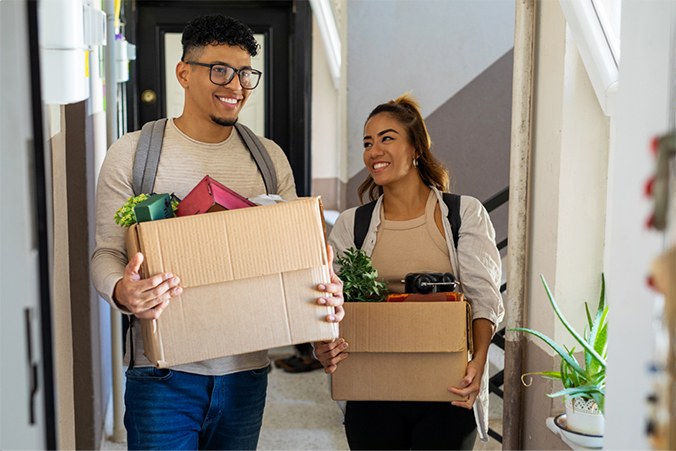 Two people carrying boxes full of items down a hallway.