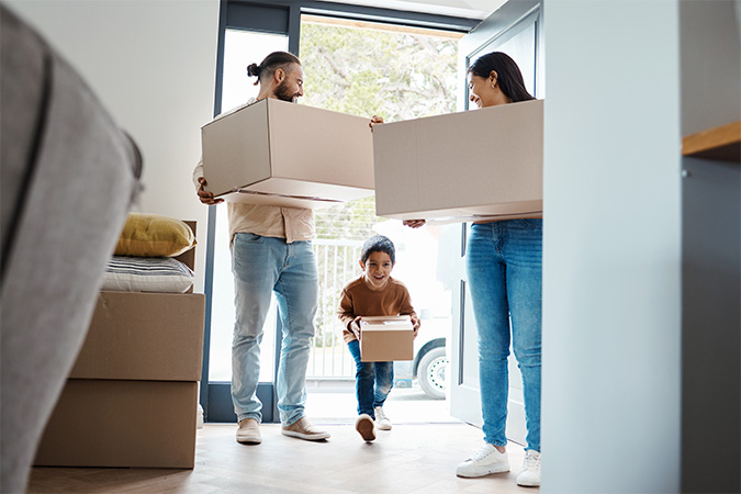 Three people carrying boxes full of items through a doorway.
