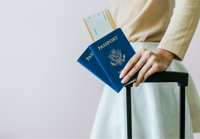 A woman in a white dress holding passports and a luggage handle.