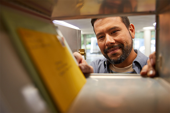 View from the back of a PO Box as a person opens it and sees mail pieces inside.